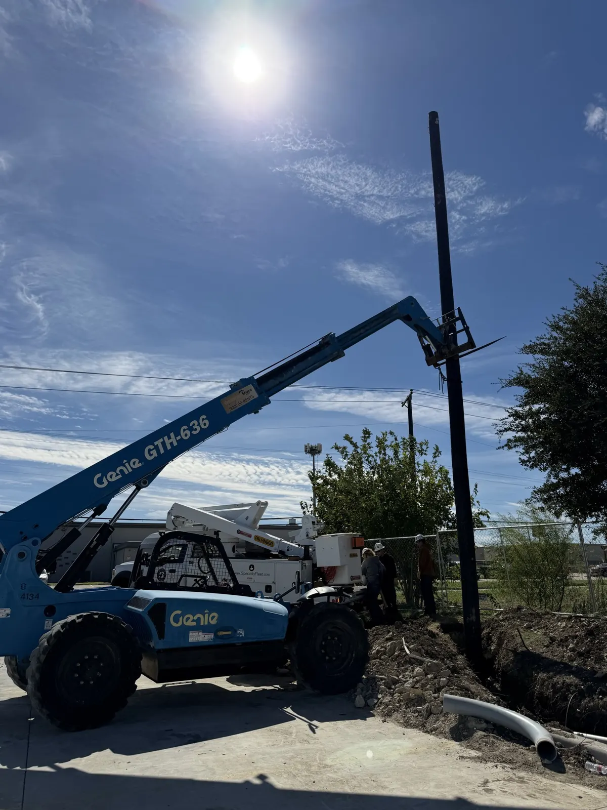 Telehandler holding a utility pole near a bucket truck at a Saginaw, TX job site